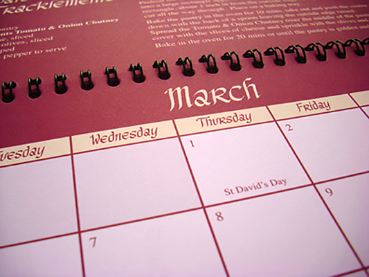 A close-up picture of a red, spiral-bound calendar that uses old-english style script